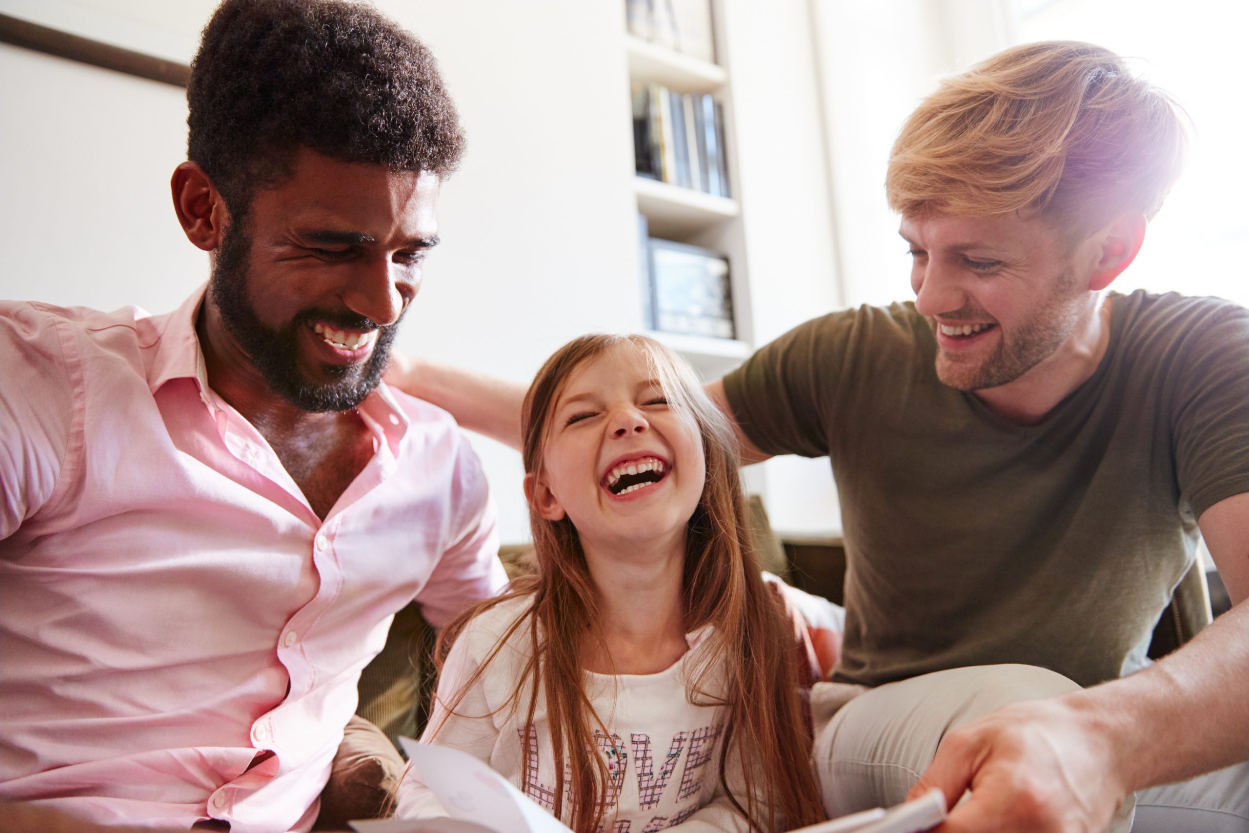 Same Sex Male Couple Reading Book With Daughter At Home Together Whilst  Tickling Her - Adoption Council of Ontario